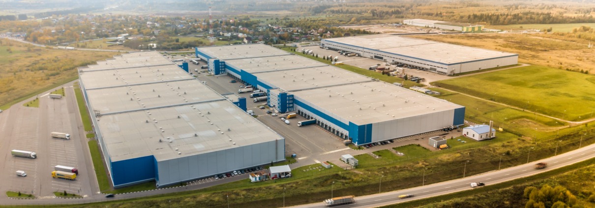 Aerial shot of industrial warehouse. Loading hub and many trucks with cargo trailers. Aerial view of goods warehouse. Modern Distribution Center from outside. Aerial view of warehouse with trucks.